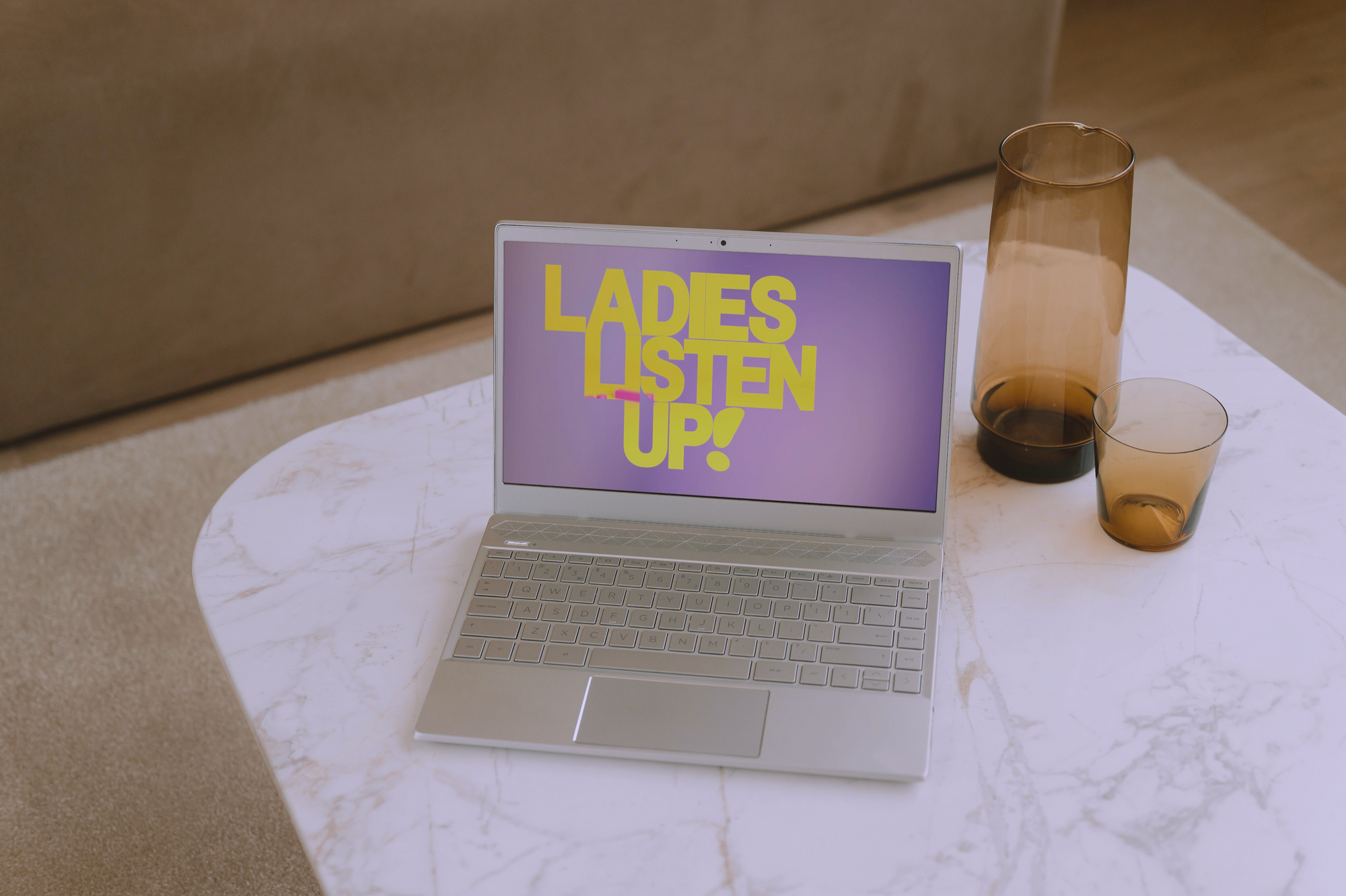 Silver laptop on marble table has the Ladies Listen Up! title screen, IndieSoup Media tv show hosted by Gwendolyn R. Houston-Jack, on the screen. 